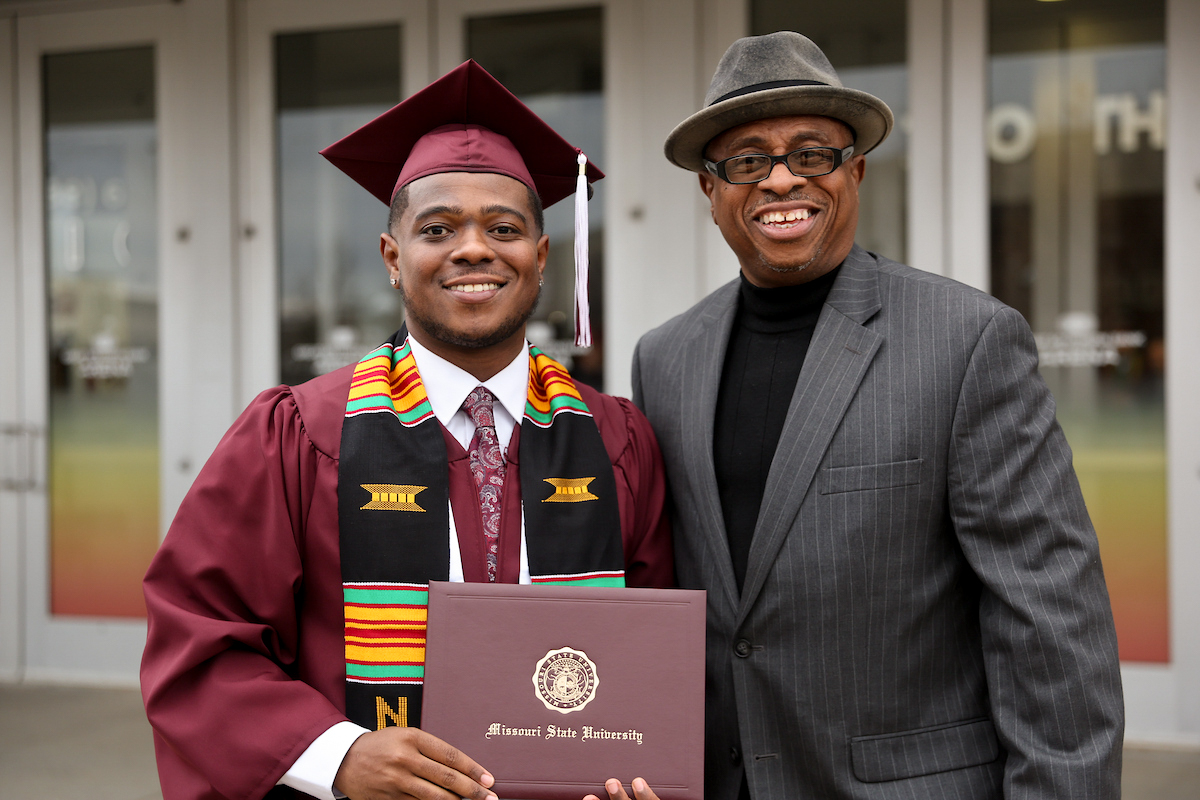 A new graduate at graduation posing with family member