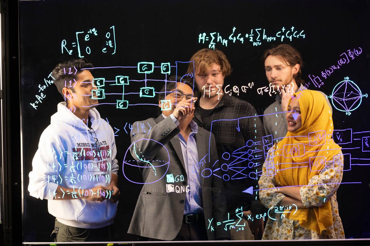 Students and professor working out a physics problem on a blackboard