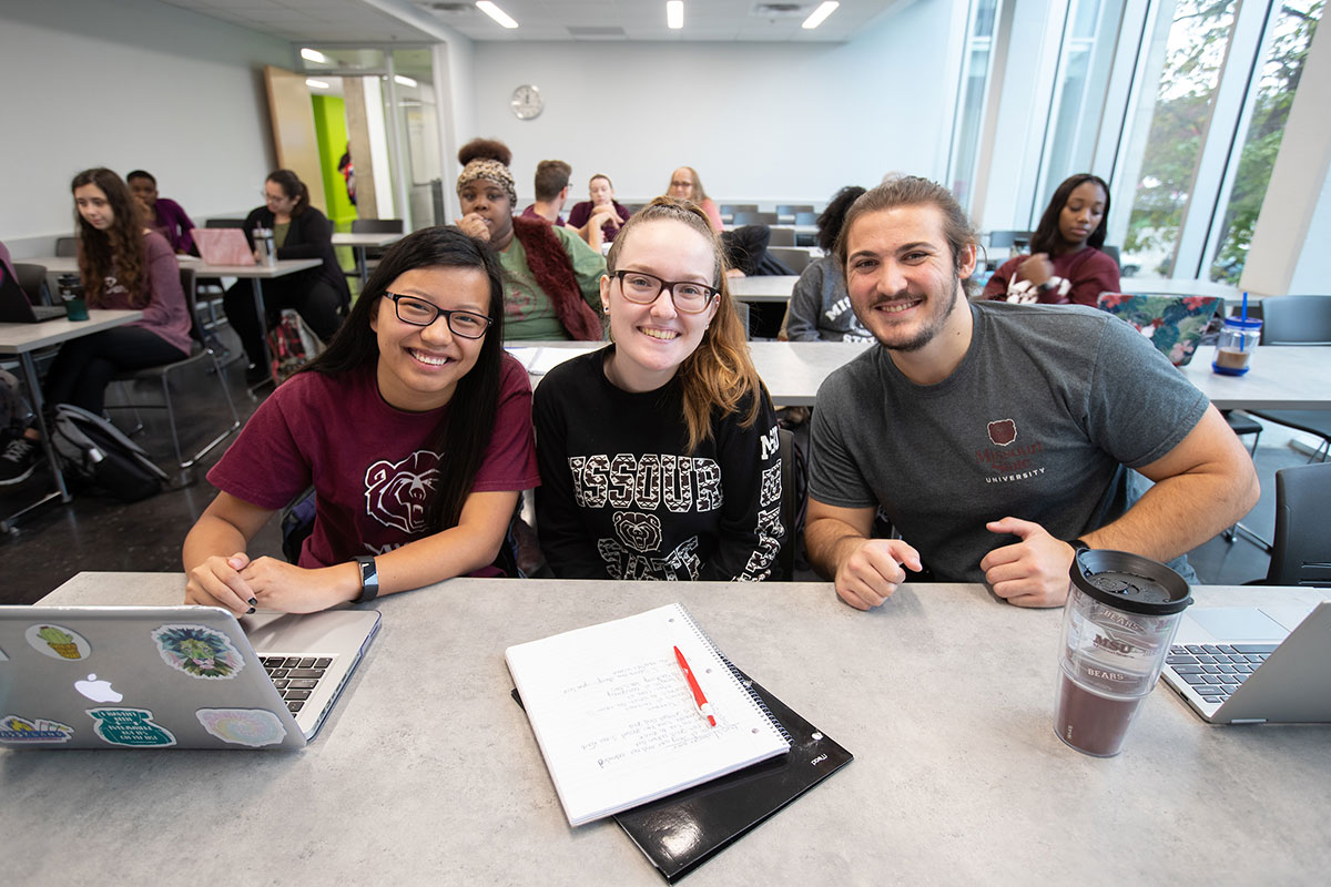 Three students posing for a photo inside a classroom