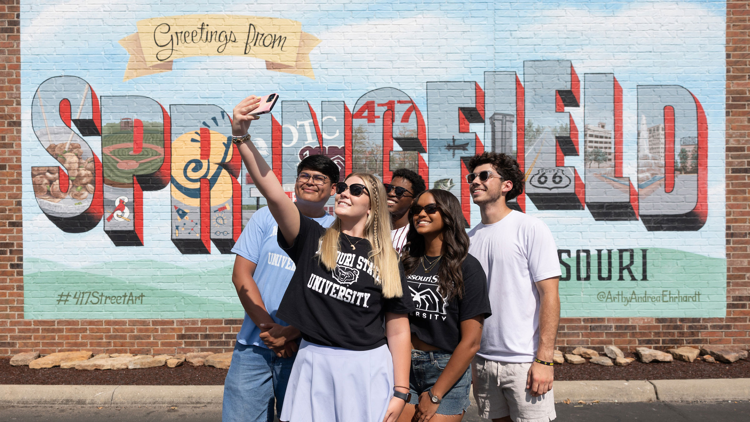 Students taking a group selfie in front of a Springfield postcard mural