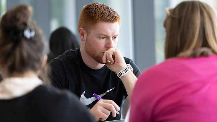 A student rests his chin in his hand while he contemplates what he needs to write.