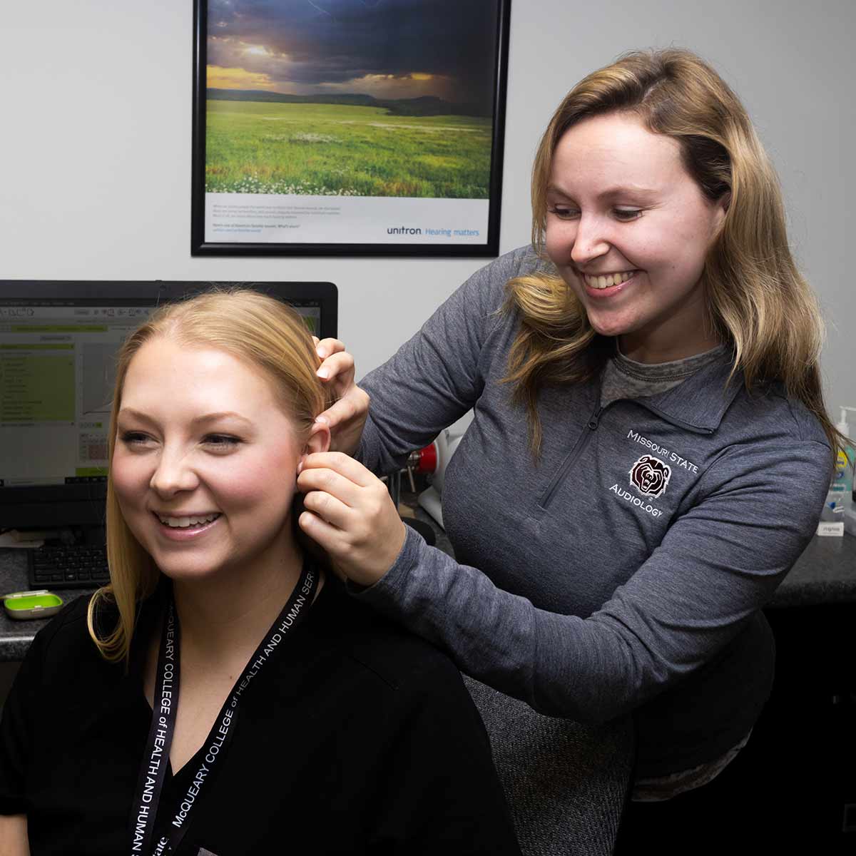 An audiology student demonstrates how to insert a hearing aid on a patient. Her patient is another student.