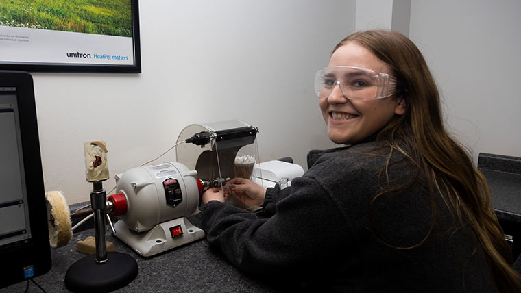 An audiology student looks back and smiles while work with a hearing aid machine.