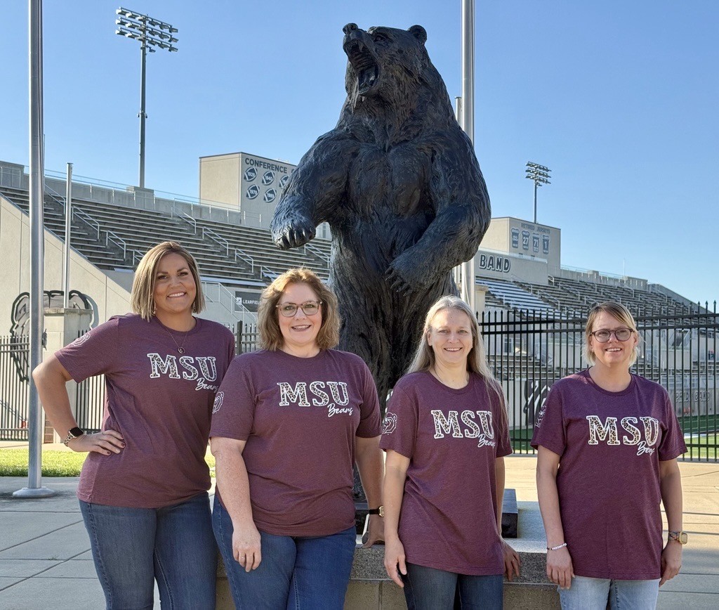 Bursar staff members standing in front of a bear statue