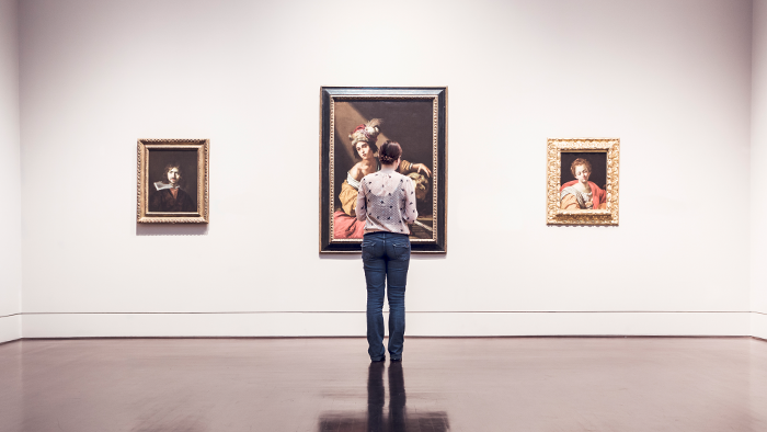 A woman inside a museum looks at a wall with portrait art