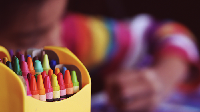 A box of crayons in front of a girl coloring