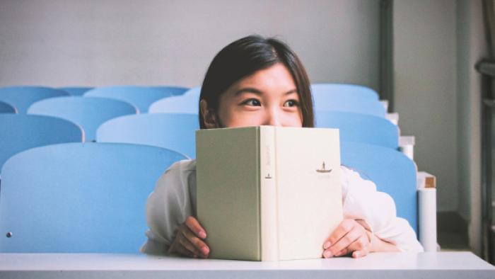 A young woman excitedly looking over the top of a book