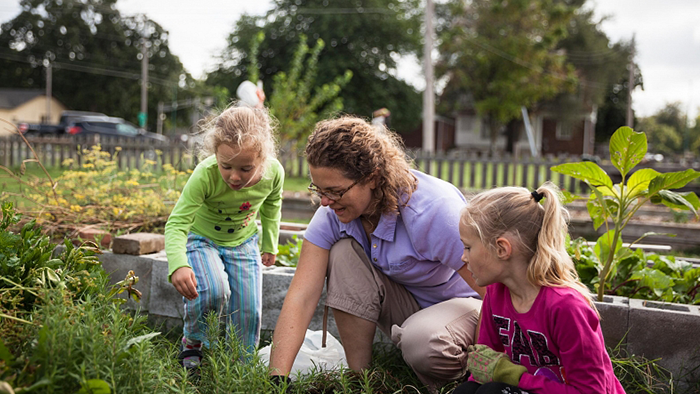 A women and two little girls tend to plants in a garden
