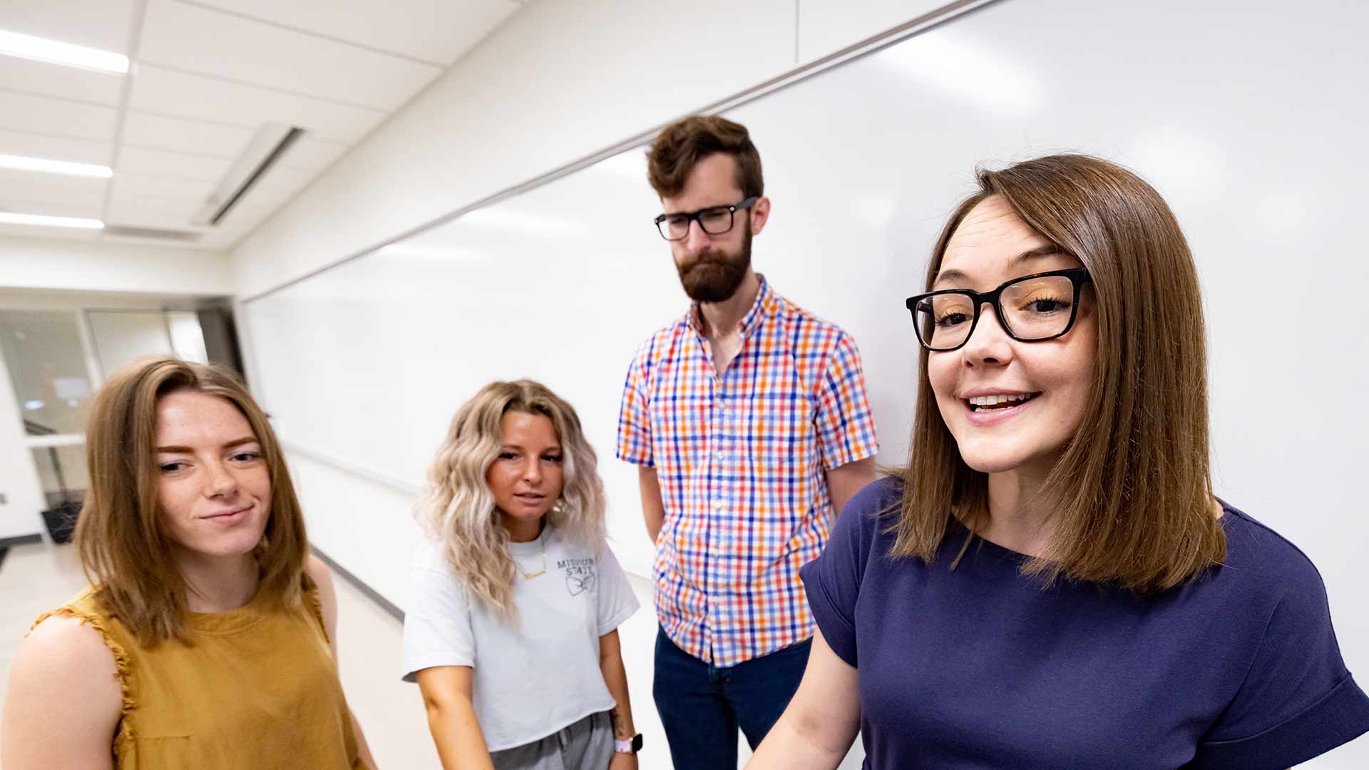 Three communication graduate students and assistant professor Dr. Carrisa Hoelscher looking at a computer screen together during class.