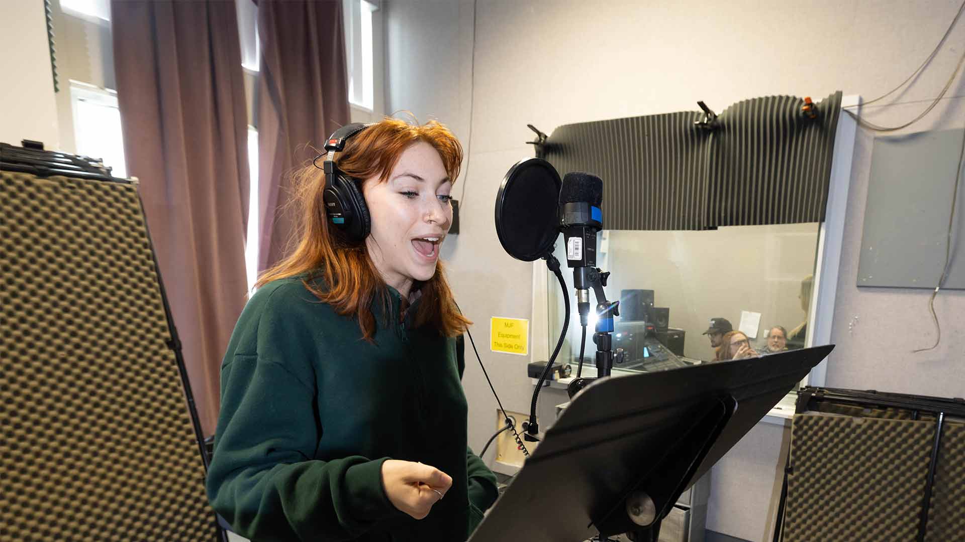 A theatre student sings in a studio while film journalism students record the audio nearby in a separate room.