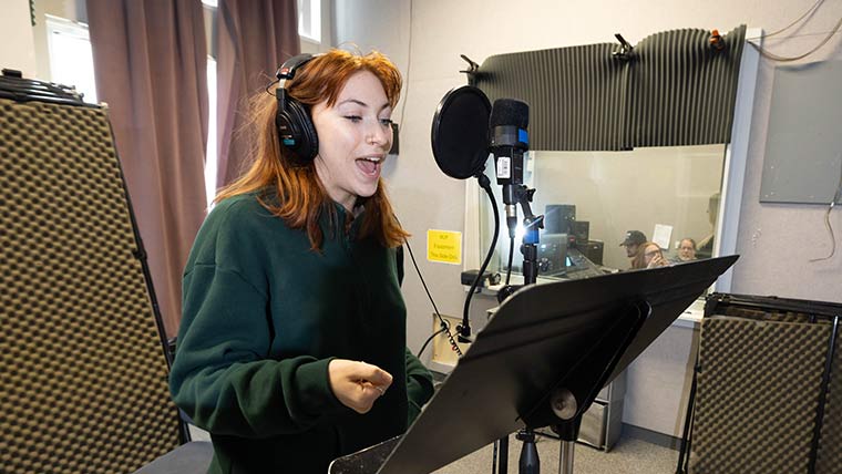 A theatre student sings in a studio while film journalism students record the audio nearby in a separate room.