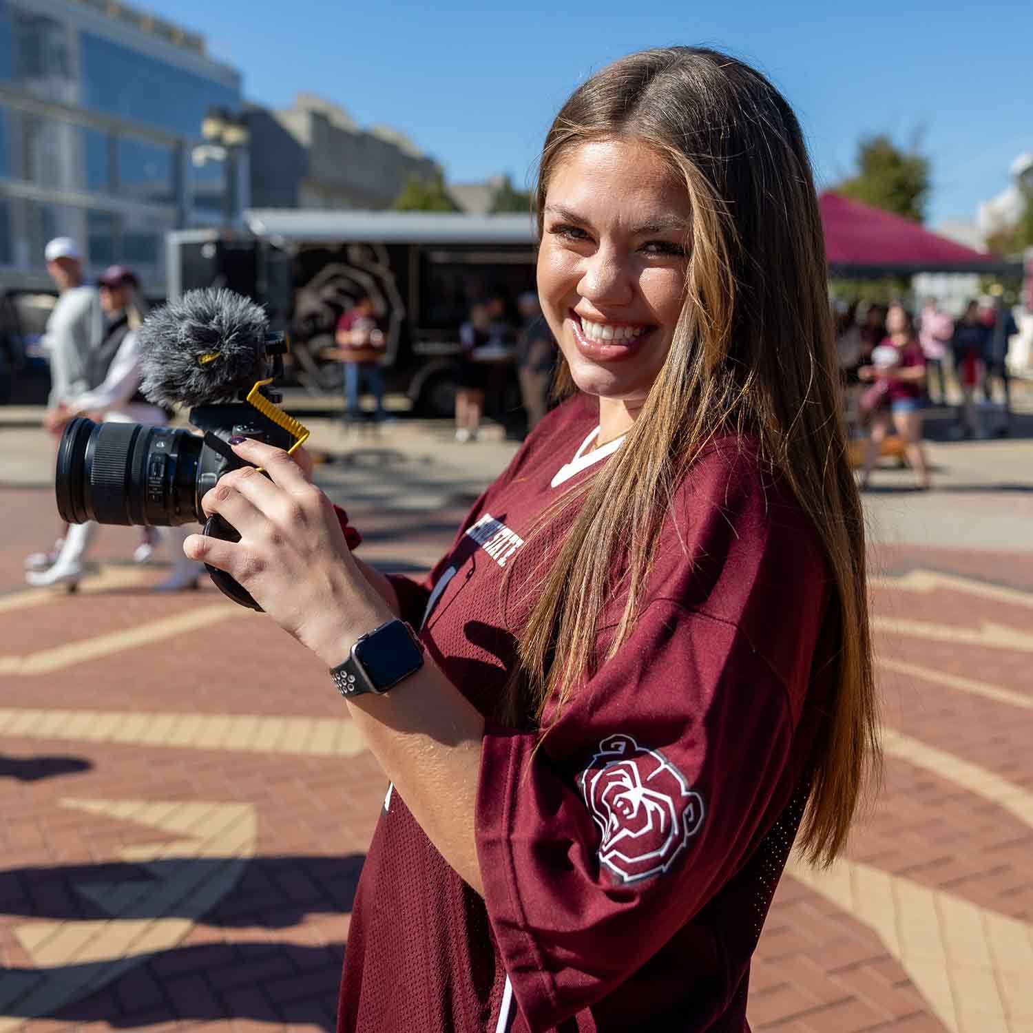 A student videographer smiling at the camera as her picture is being taken.