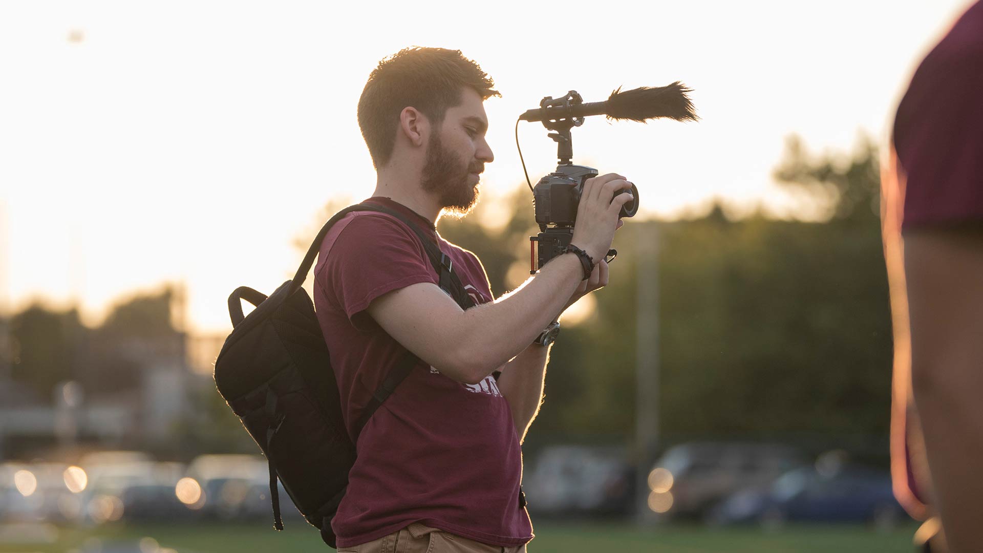 A student videographer records video at a campus event during sundown.