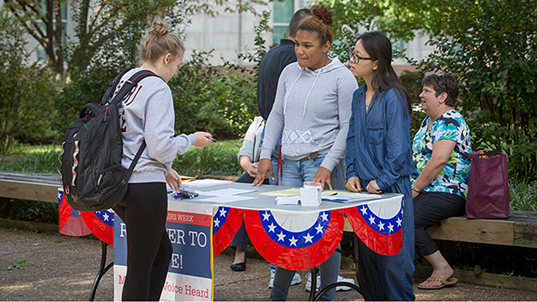 Two students manage a booth as they assist a student who is registering to vote.