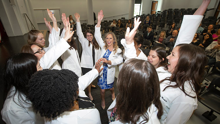 A group of audiology students do a high-five together after their white coat ceremony.