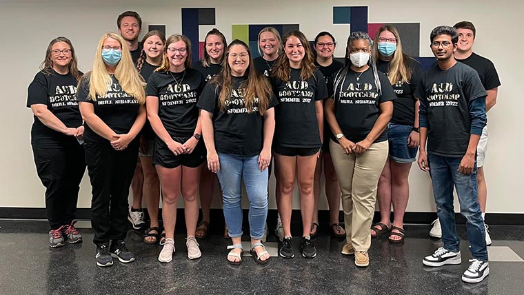 A group of audiology students and faculty wearing black T-shirts for a hearing aid bootcamp. Their shirts say "AUD Bootcamp Summer 2022"