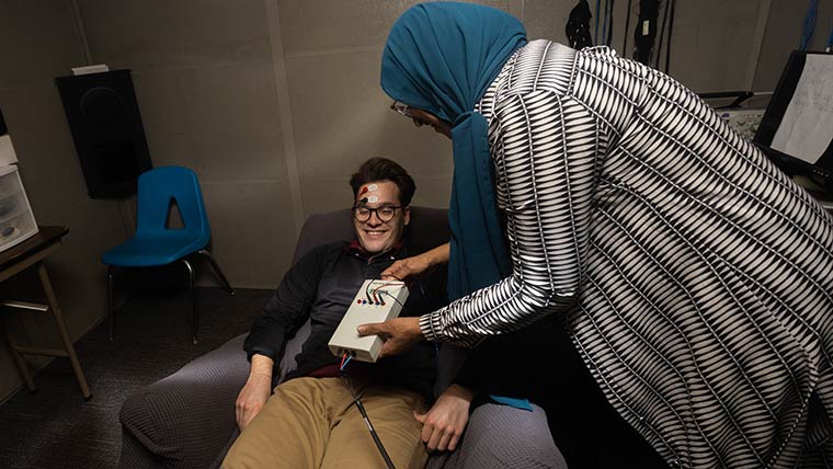 An audiology professor connects equipment to a student's head during a lab demonstration.