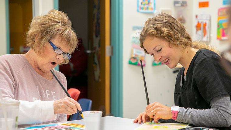 A speech-language student paints with an adult patient during a group therapy session.