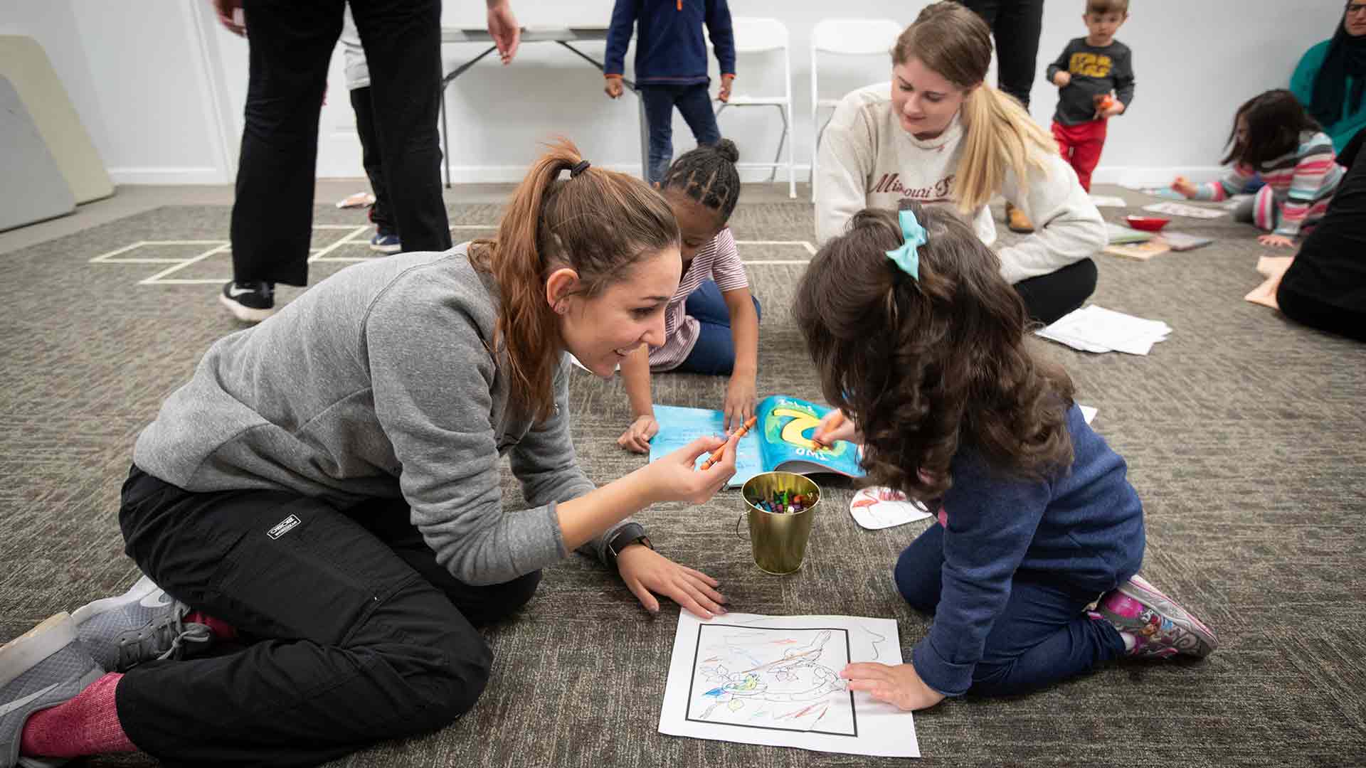 A speech-language student and a young child color together on a sheet of paper during a community event.