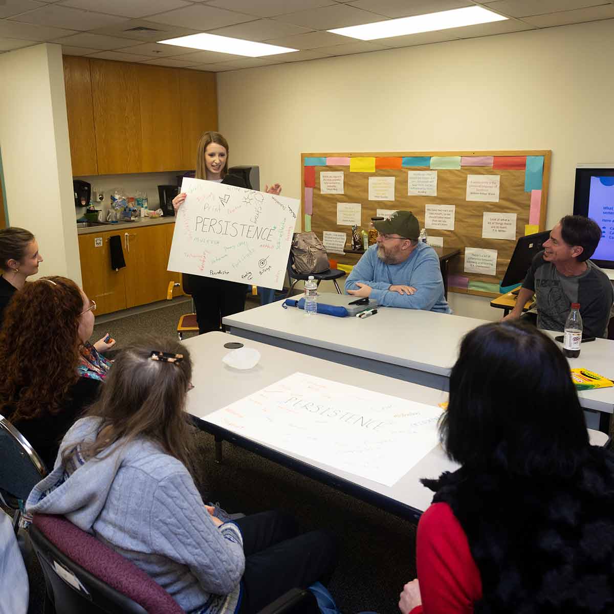A speech therapy student holds up a sign in front of clients during an adult group therapy session