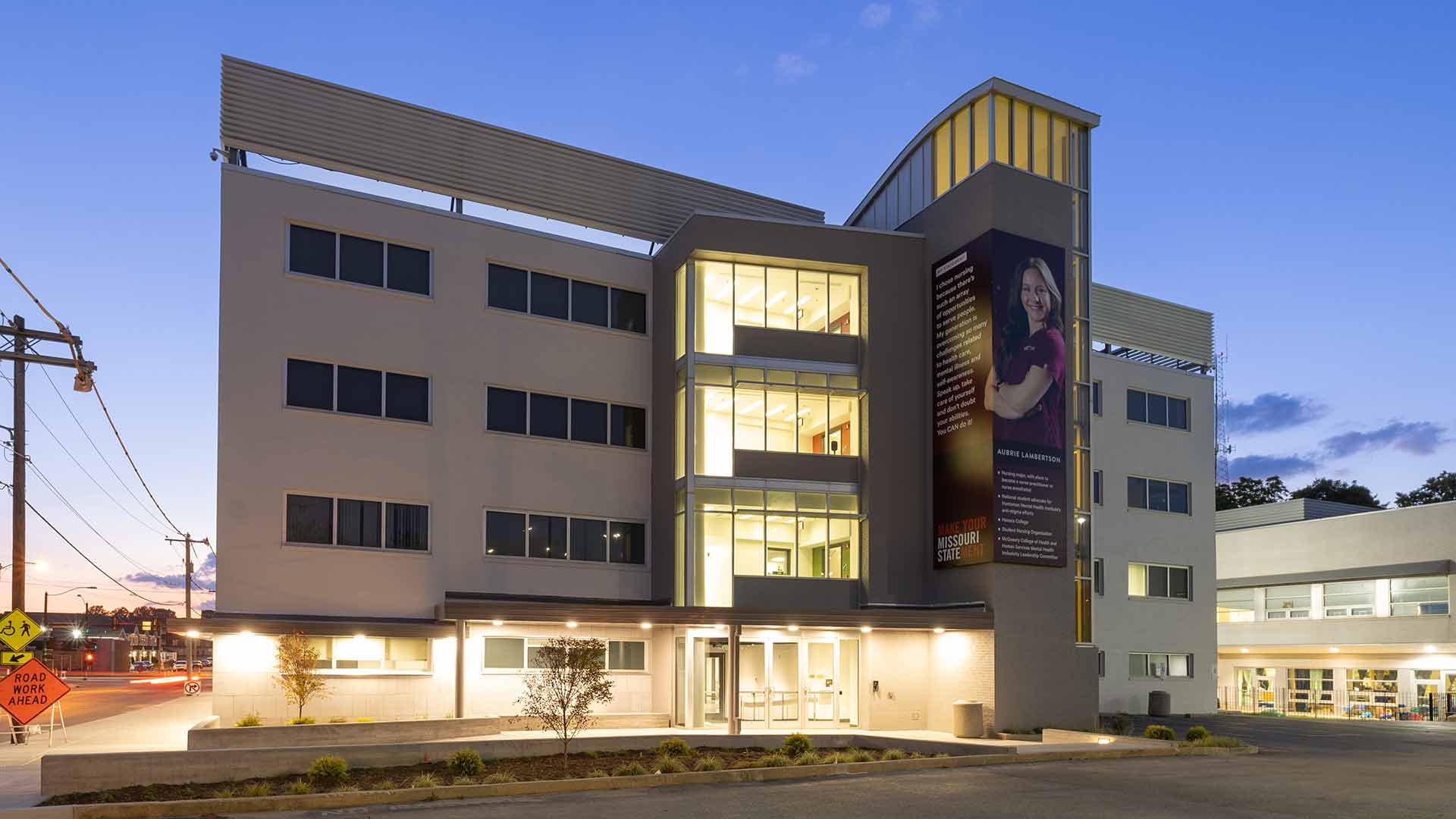 The renovated Ann Kampeter Health Sciences Hall with lights on at dusk.