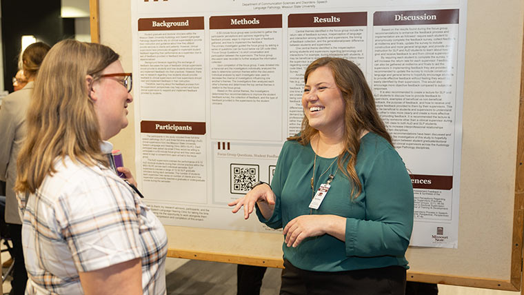 A speech-language therapy student talks to a professor during the graduate research forum.