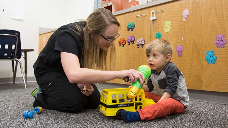 A speech-language student does a therapy session with a young child in a play area.