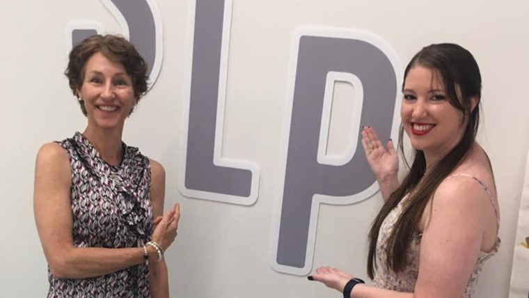 A student and professor pointing to the letters "SLP on the wall behind them.
