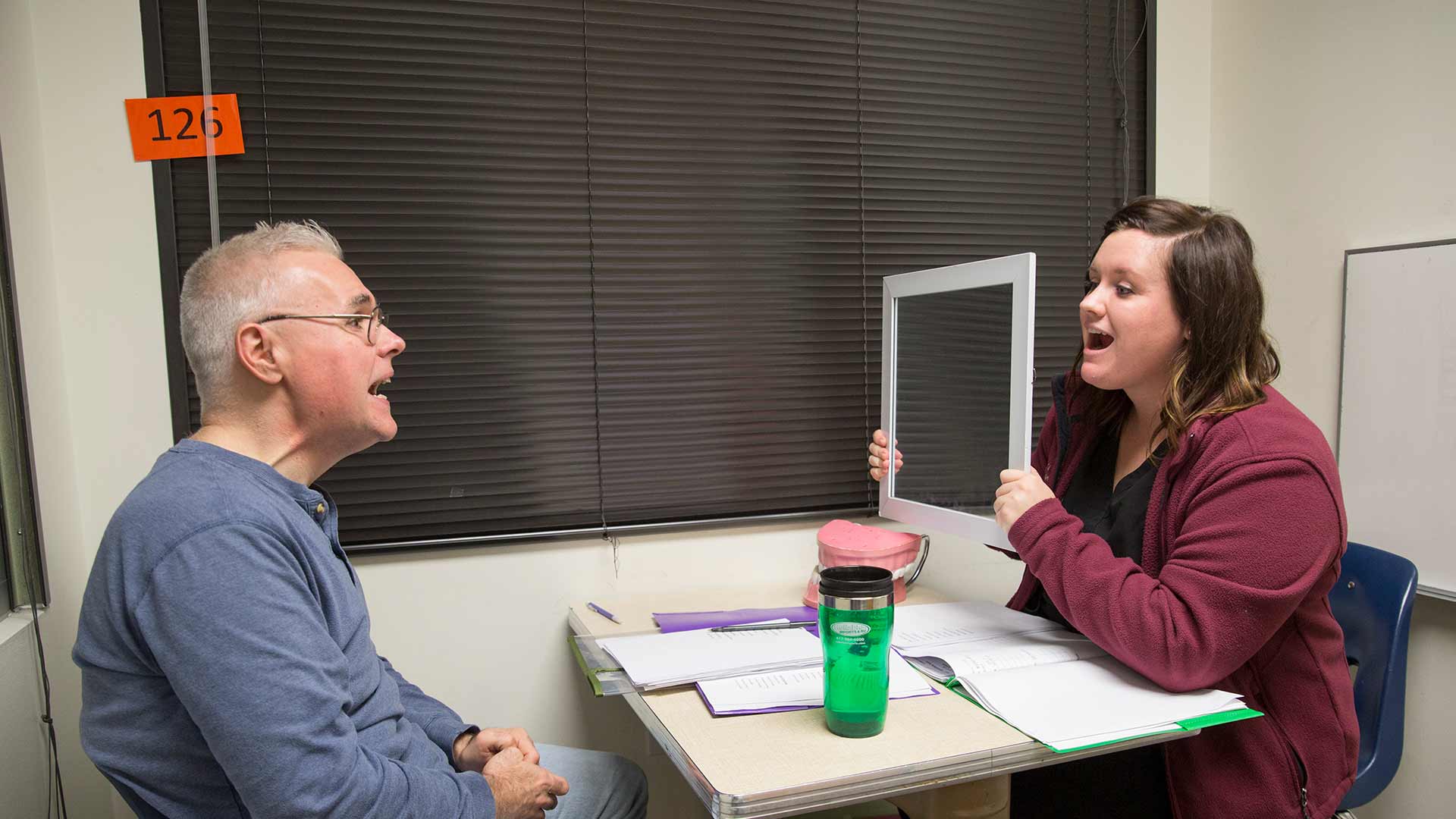 A speech-language student holds up a tablet in front of a client during a therapy session.