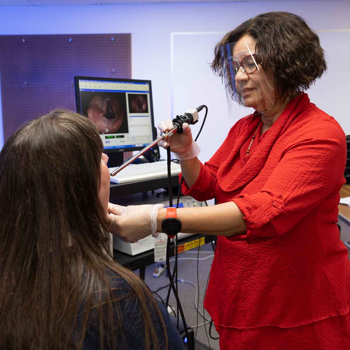 A speech-language pathologist demonstrates how to do a throat scope on a patient.