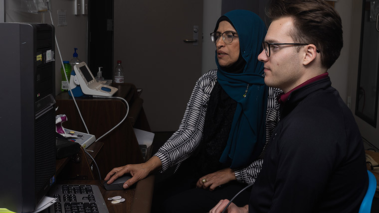 An audiology student and professor look at computer data while in a lab.