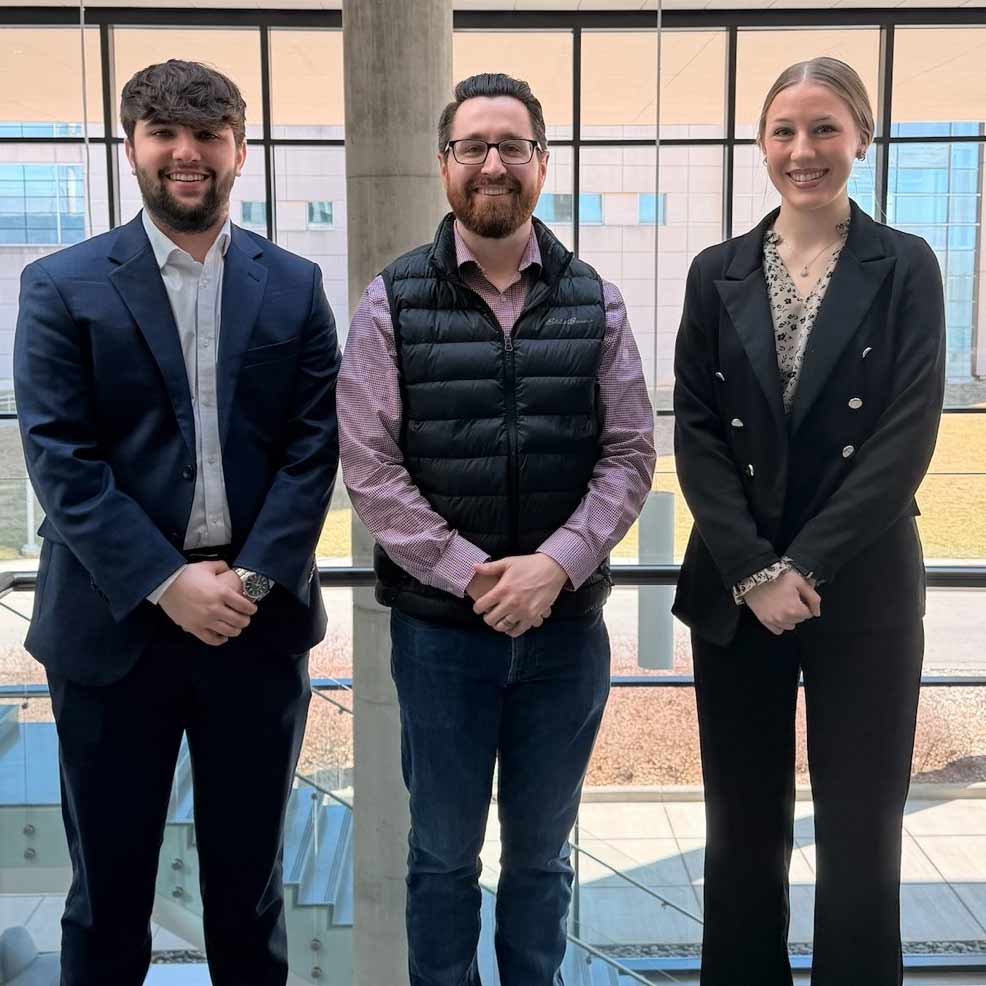 Two students with a financial planning professional in a corporate office.