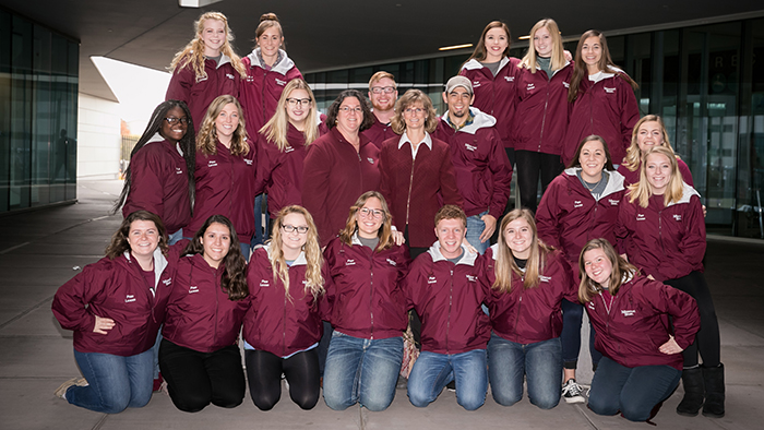 A posed shot of a group of people wearing matching maroon jackets
