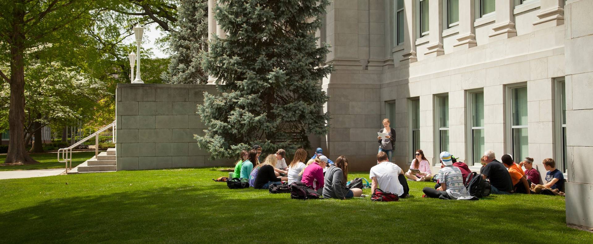 Group of students sit outside of neoclassical building for class.