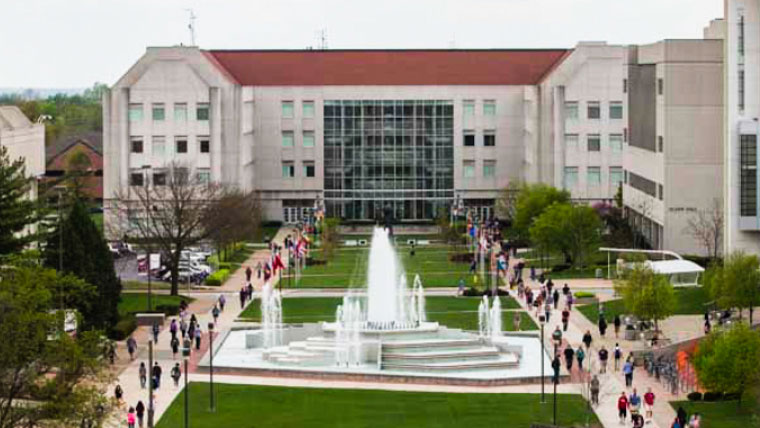 An overhead view of a university campus plaza featuring a large, active water fountain, walkways with pedestrians, and the Strong Hall building in the background