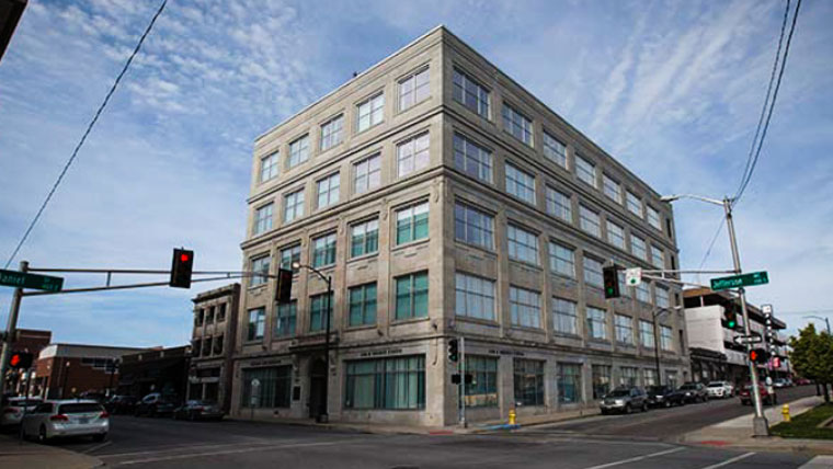 A multi-story, grey stone building known as the Jim D. Morris Center, located on a city street corner under a blue sky with light clouds
