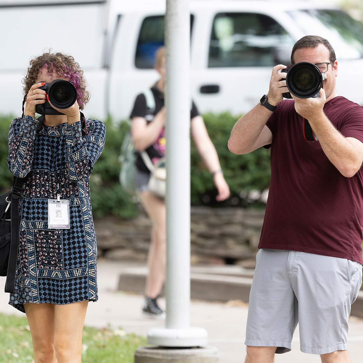 Two staff photographers holding up their cameras at the person taking the photo.
