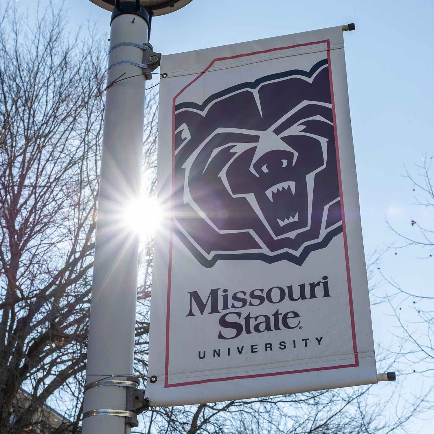 A Missouri State University banner with the Bear head logo hanging from a light pole on campus.