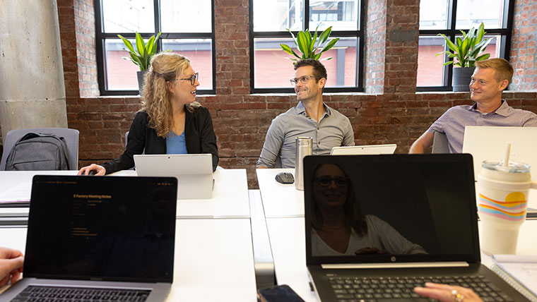 Professionals at the efactory chat at a long table with laptops and computer tablets on the table in front of them.