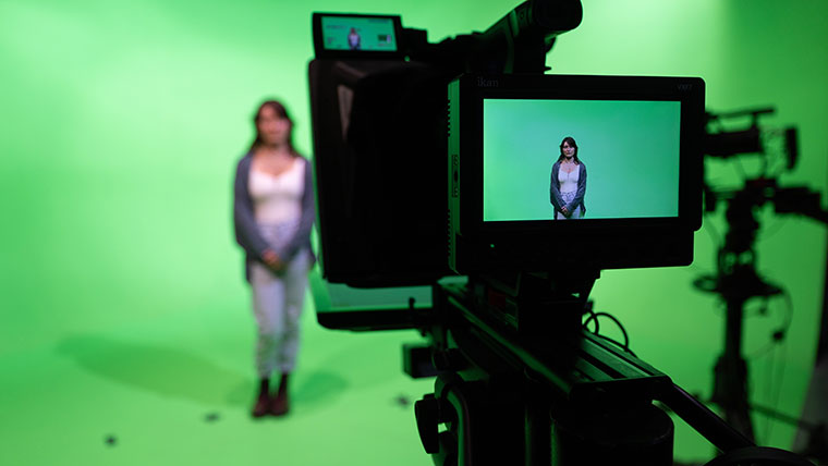 An RCASH student stands in front of a green screen as a camera takes a video of her.