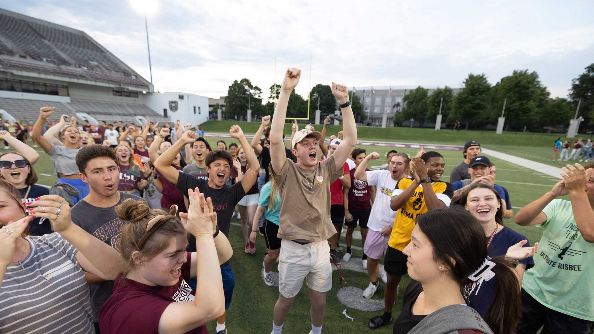 Missouri State students standing on the football field cheering. 