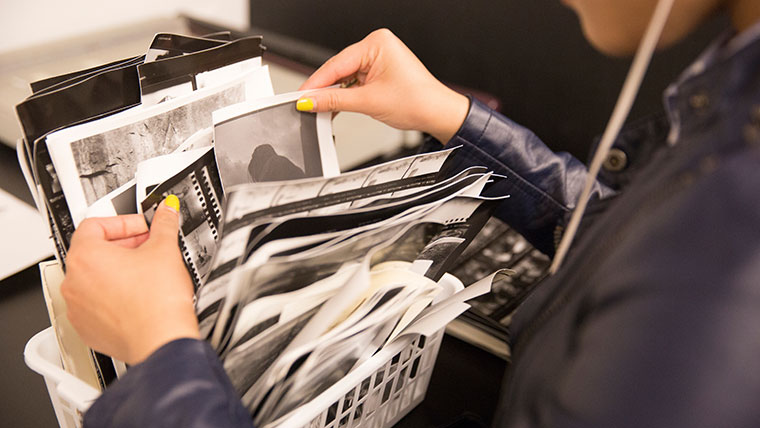 An art student rummages through a container of black and white photos.