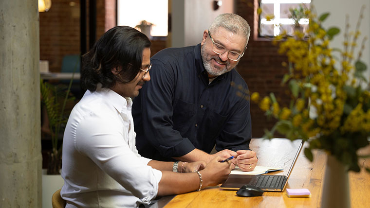 Two professionals have a discussion while searching the web on a laptop.