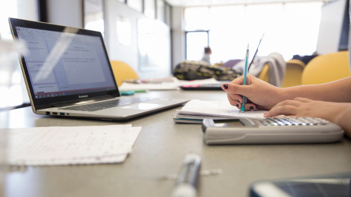 A student writes notes while viewing a laptop computer