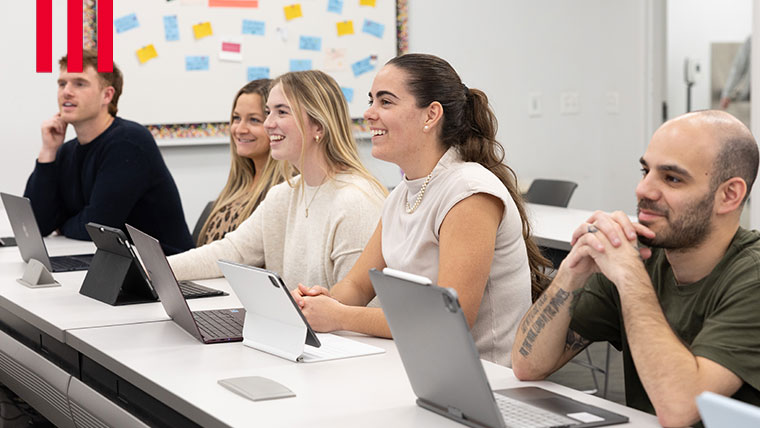 A group of sitted students smiling within a classroom.