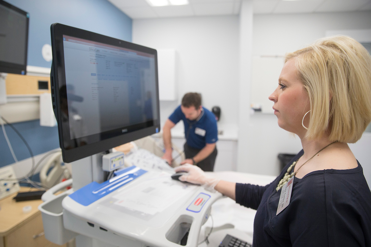 Students in simulation lab standing at a monitor and interacting with a mannequin patient 