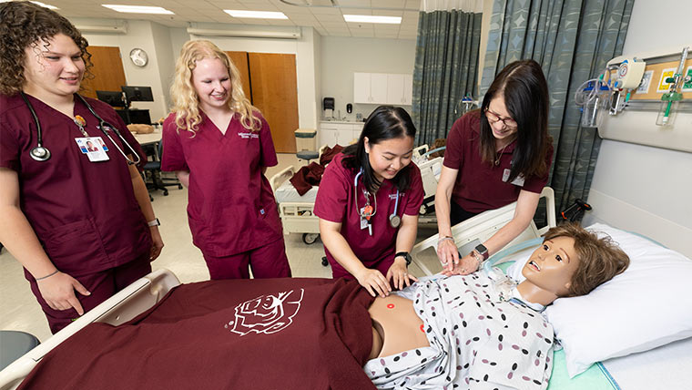 A group of nursing students and professor working with a manikin in the sim lab.