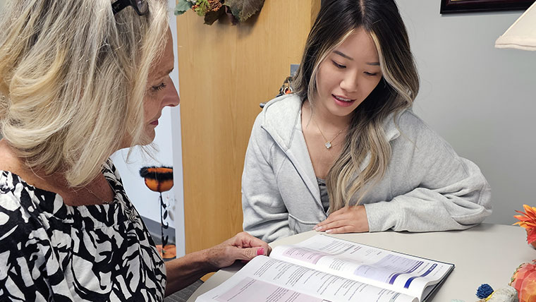 Nurse faculty assisting a nursing student while reviewing a book. 