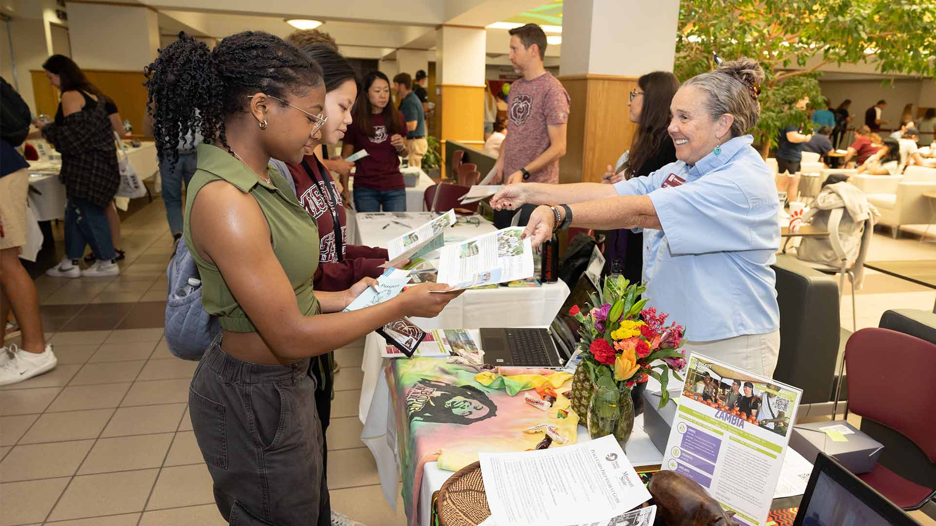 Two students receive brochures from a faculty member during an Education Abroad fair in the Plaster Student Union.