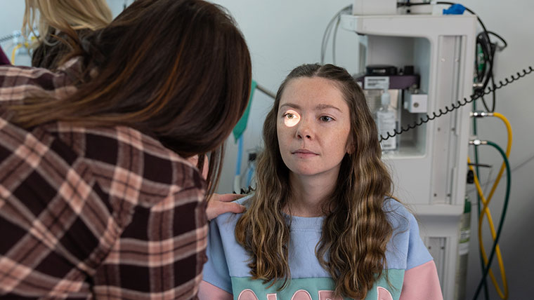 A nursing student shines a light into her classmate's right eye during a practice eye exam.